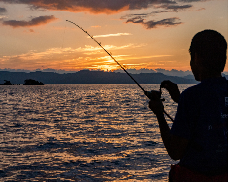 夕日を背に船の上で釣り糸を垂れる子ども